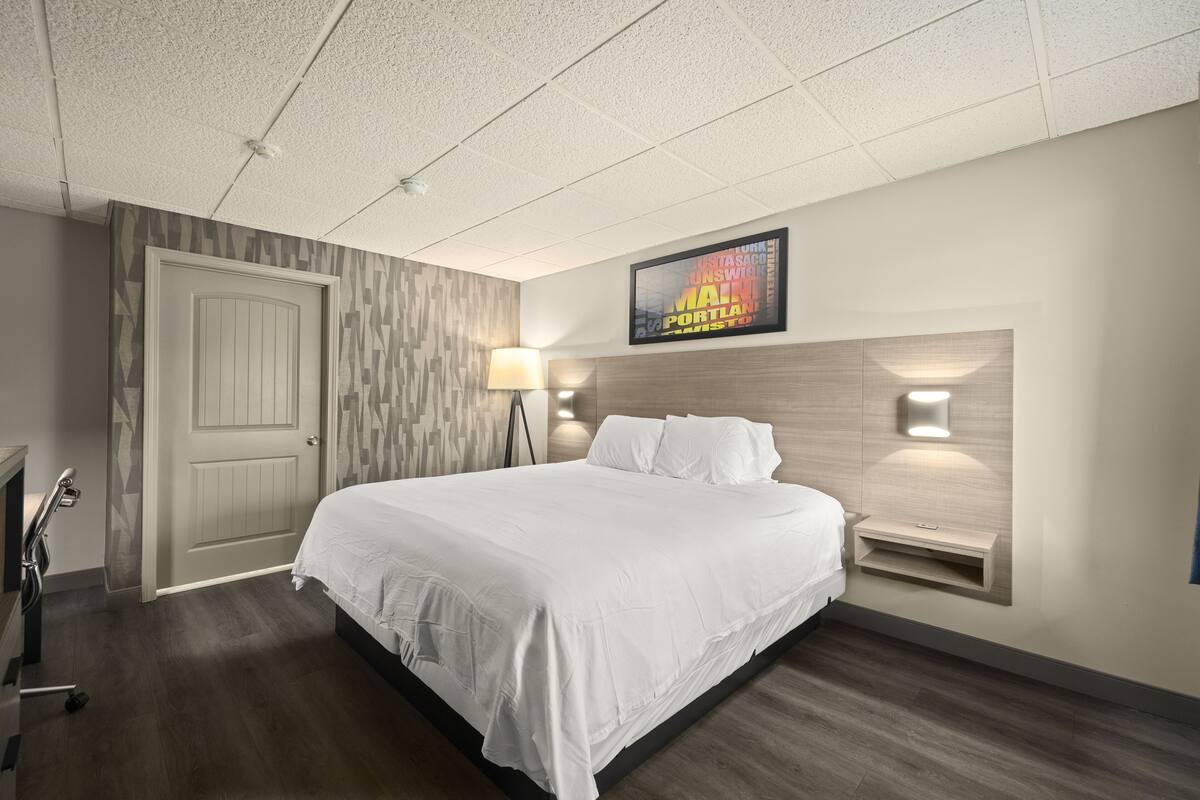 A hotel room with a large bed, a headboard with integrated lighting, a wall-mounted TV, and a bedside table.