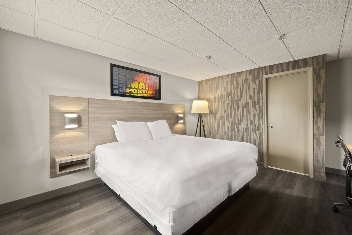 A hotel room with a large bed, a headboard with a built-in shelf, a wall-mounted TV, and a lamp.