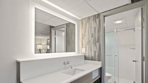 A modern bathroom with a large mirror, a white sink, and a glass shower enclosure.