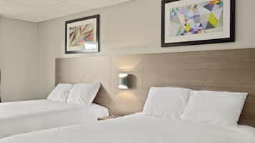 A hotel room with two beds, a wooden headboard, a wall-mounted light, and two framed artworks.