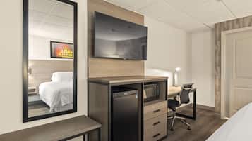A hotel room with a bed, a desk with a computer, a TV, and a minibar.