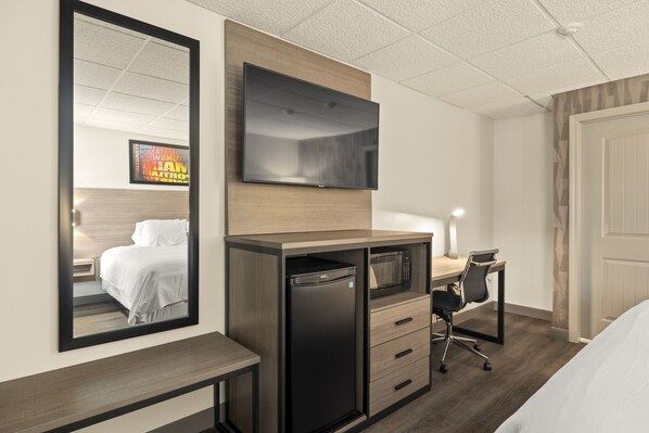 Habitación de hotel con cama, escritorio, computadora, televisor y minibar.