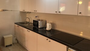 Cozinha com armários brancos, bancada preta, pia, torradeira e chaleira.