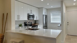 A modern kitchen with white cabinetry, stainless steel appliances, and a central island with stools.