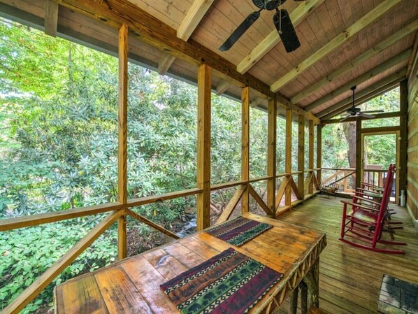 Une terrasse en bois, agrémentée d’une table et de chaises, entourée d’une balustrade en bois, et offrant une vue sur une zone boisée.