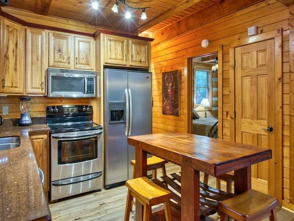 A kitchen with wooden cabinets, a stainless steel refrigerator, a microwave, and a stove. There is a wooden table with benches.