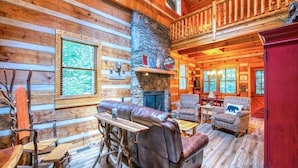 A log cabin interior with a stone fireplace, wooden furniture, and a balcony. - Twin Creeks Refuge, a log cabin, Pet friendly (Maggie Valley)