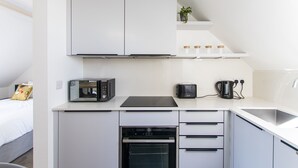 A compact kitchen with a microwave, toaster, and coffee maker on the countertop, a built-in oven below, and a sink to the right. - Bright & Beautiful Studio Flat in Bristol (Bristol)