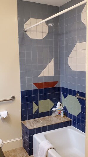A bathroom with a bathtub, a handrail, and a shelf with toiletries.