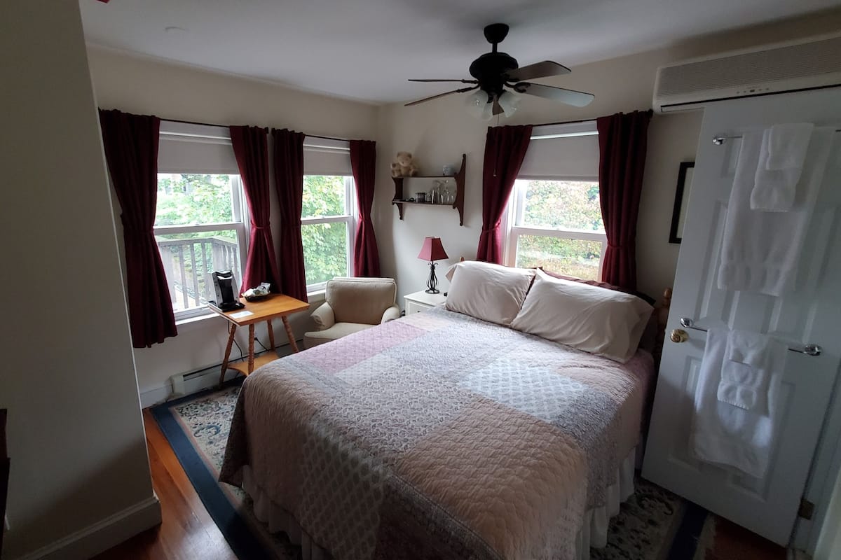 A bedroom with a bed, a desk, a chair, a ceiling fan, and a window with curtains.