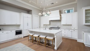 A spacious kitchen with white cabinetry, a central island with stools, a built-in oven, and a pendant light.
