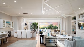 A spacious living area with a large window overlooking a scenic view, a dining area with white furniture, and a kitchen with white cabinets.
