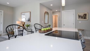 Una cucina moderna con isola centrale, sedie nere e un mobile contenitore in legno con mele.