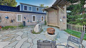 A stone patio with a fire pit, outdoor furniture, and a wooden pergola.
