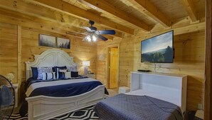 A wooden cabin bedroom with a bed, a ceiling fan, a TV, and a patterned rug. - Incredible Vibes & Views #204 (Sevierville)