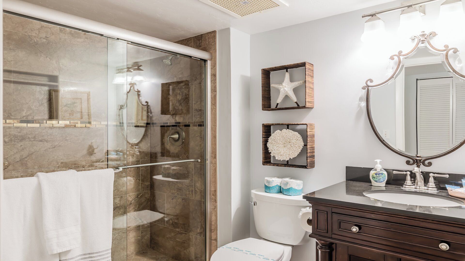 Une salle de bain avec une douche en verre, des toilettes, un meuble-lavabo avec un miroir et des étoiles de mer décoratives accrochées au mur.