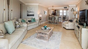 Un salón espacioso con un sofá color beige, una mesa de centro y un comedor con una cocina al fondo.