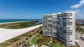 Un hotel moderno de gran altura con múltiples balcones, un jardín ajardinado y vistas a la playa y al océano.