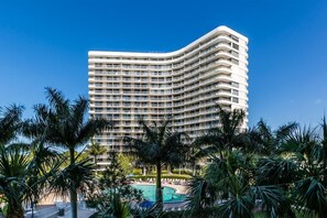 Un hotel moderno de gran altura con varios balcones, una piscina y palmeras al frente.