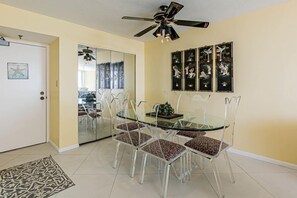 Un comedor con una mesa de vidrio y sillas, un ventilador de techo y obras de arte en la pared.