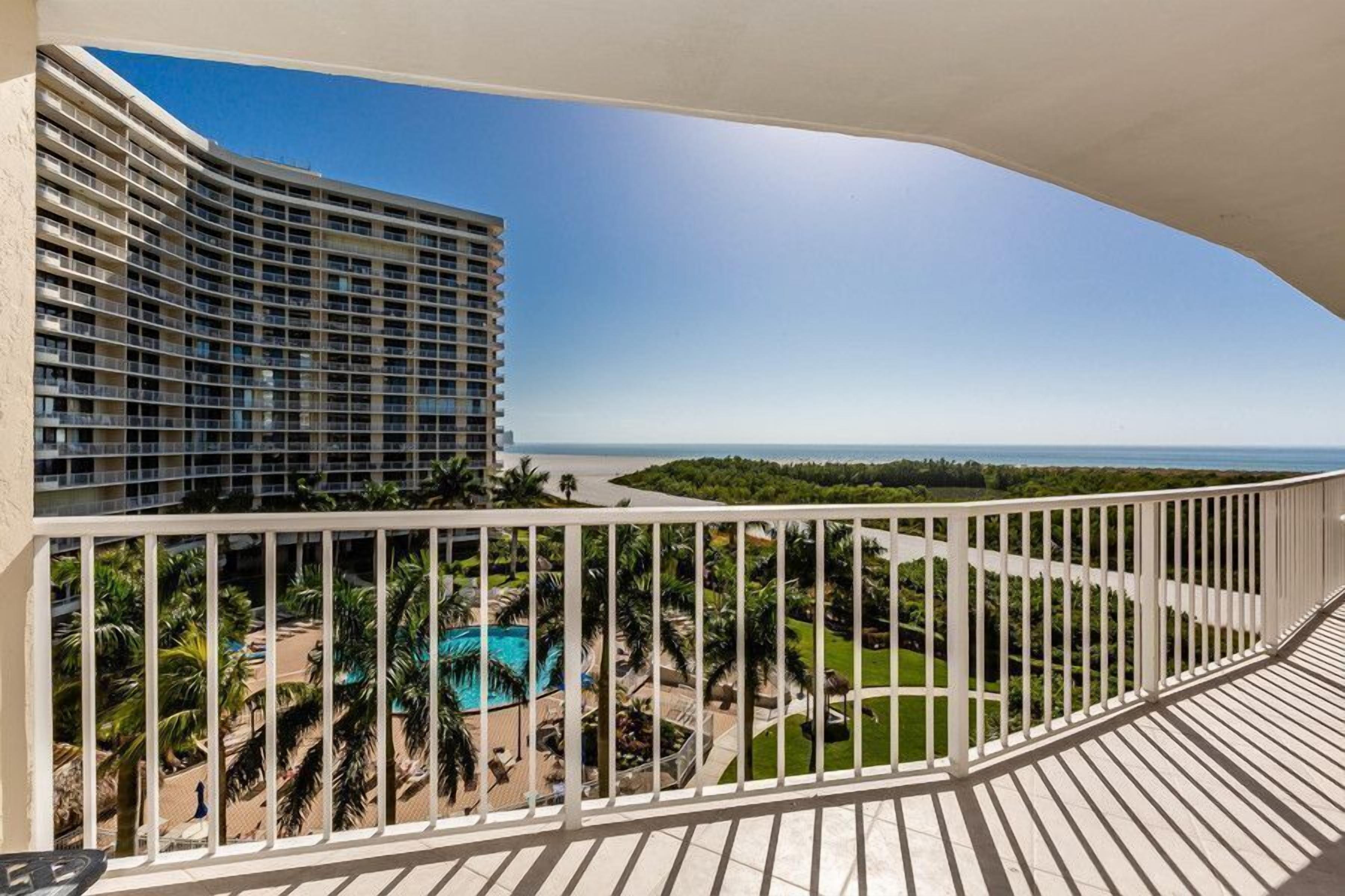 A balcony with a view of a hotel, a pool, and a beach.