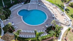 A circular pool with a heart-shaped design, surrounded by lounge chairs and palm trees. - This 2/2 condo is just steps away from the beach (Marco Island)