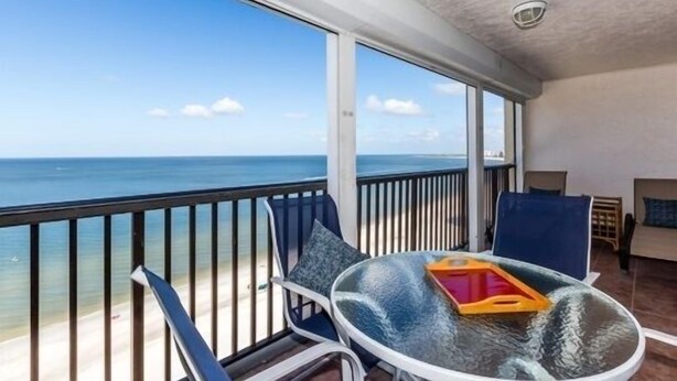 Un balcon avec une table en verre, des chaises et une vue sur l’océan.