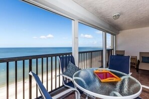 Een balkon met een glazen tafel, stoelen en uitzicht op de oceaan.