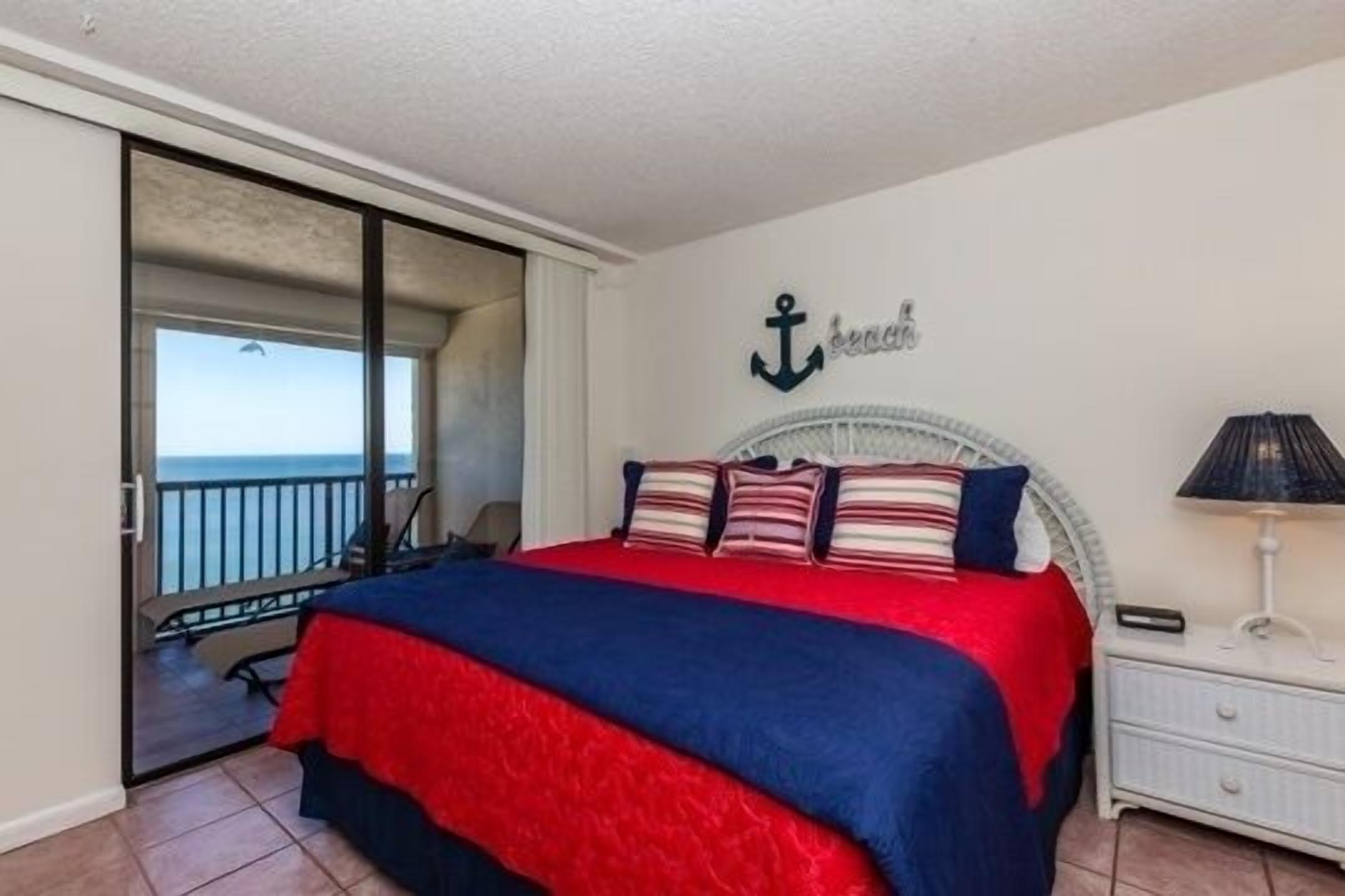 A bedroom with a bed, a nightstand, and a view of the ocean through a sliding door.