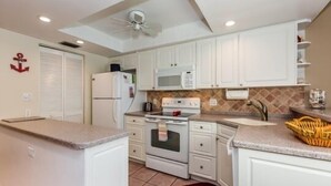 Une cuisine de taille réduite, avec des meubles blancs, un four à micro-ondes, une cuisinière et un réfrigérateur.