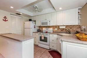 A compact kitchen with white cabinets, a microwave, a stove, and a refrigerator.