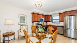 Una cocina moderna con armarios de madera, electrodomésticos de acero inoxidable y una zona de comedor con sillas de mimbre y una mesa de vidrio.
