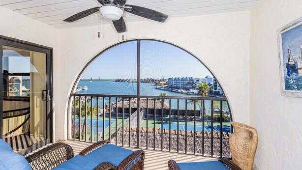 A balcony with wicker furniture, a view of a marina, and a ceiling fan.