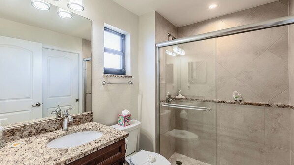 A bathroom with a granite countertop sink, a glass shower enclosure, and a white toilet. - Lovely 1BR/1BA condo with a spectacular Bay View (Marco Island)