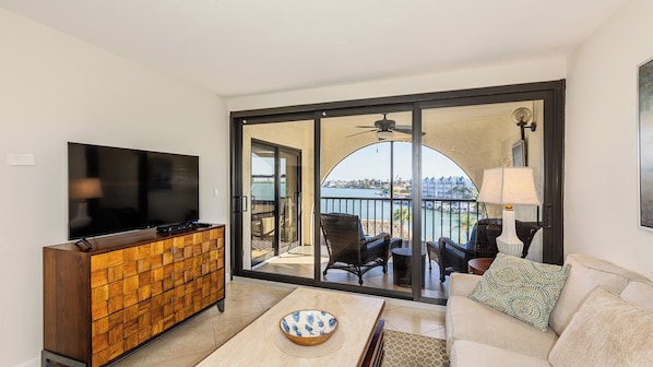 A living room with a flat-screen TV, wooden cabinet, sofa, and a view of a body of water through a glass door.