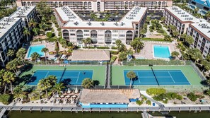 An aerial view of a hotel with two tennis courts, a pool, and a beach area with umbrellas. - Lovely 1BR/1BA condo with a spectacular Bay View (Marco Island)