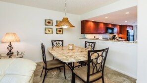 Un coin repas avec une table en marbre, quatre chaises, un luminaire suspendu et une cuisine visible au fond.