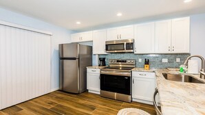 A modern kitchen with white cabinets, stainless steel appliances, and a wooden floor. - Lovely 2 bedroom 2.5 bath condo (Marco Island)