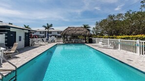 A rectangular swimming pool with clear blue water, surrounded by lounge chairs and a thatched-roof structure.
