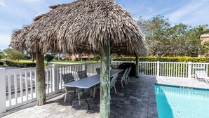 A poolside area with a thatched umbrella, outdoor seating, and a swimming pool. - Lovely 2 bedroom 2.5 bath condo (Marco Island)