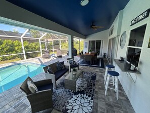 Un espace aménagé au bord de la piscine, avec des meubles en osier, un bar et une pancarte indiquant « BIENVENUE ».