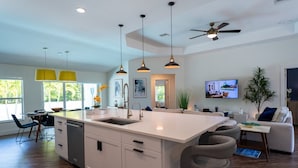 A modern kitchen with a central island, pendant lighting, and a ceiling fan.