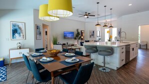 A modern kitchen with a central island, bar stools, and a dining area with a wooden table and blue chairs.