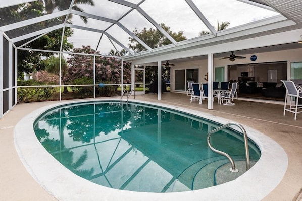 An indoor swimming pool with a glass ceiling, surrounded by a covered patio area with seating and a bar.
