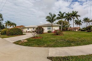 A single-story house with a front yard, palm trees, and a driveway.