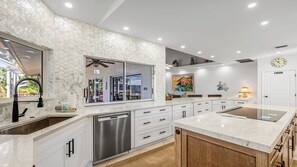 A modern kitchen with a large island, white cabinetry, and a dishwasher.