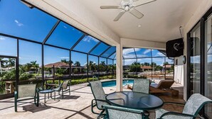 A covered outdoor area with a pool, seating, and a ceiling fan.