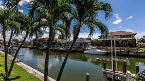 A marina with a dock, palm trees, and a house in the background.