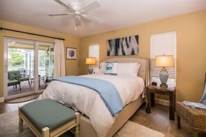 Relax in this serene bedroom with a large bed, ceiling fan, and two bedside lamps, plus a sliding door to an outdoor area with comfortable seating.
