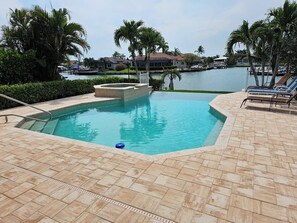 Une piscine dont le fond est revêtu de carreaux disposés en motif « point de Hongrie », un jacuzzi et des chaises longues.